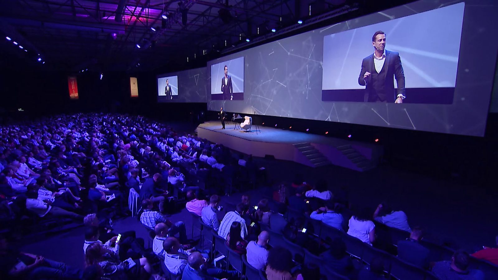 Gilan on stage in a packed auditorium, shown on the big screens